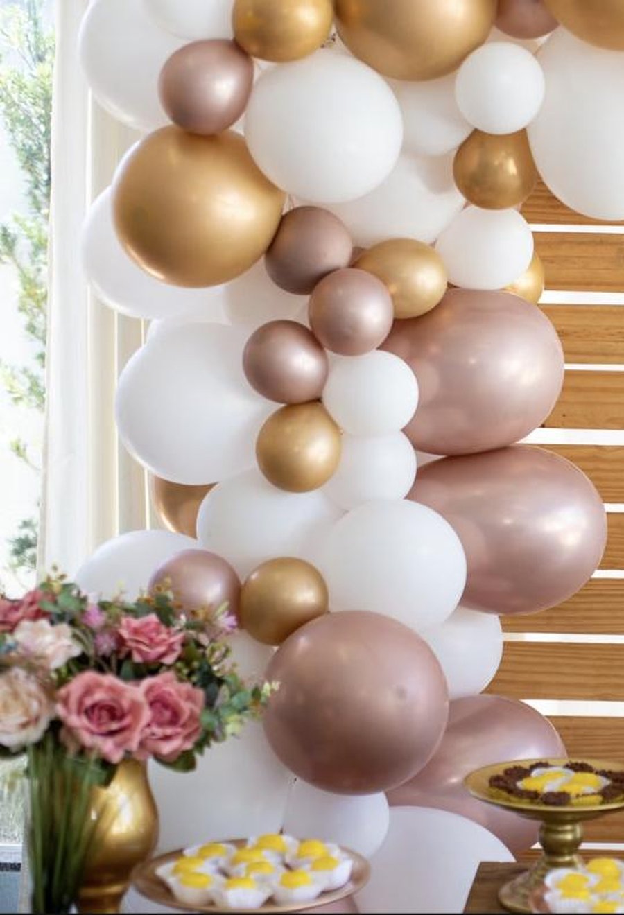 Rose gold, white and champagne balloon garland cascading over a styled birthday table