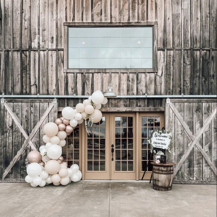 Neutral balloon garland framing rustic barn doors at a wedding